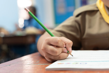 Close up of student hand holding pencil writing on paper in classroom, concept of education learning...