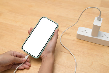 Close up of a person charging smartphone via USB cable. Blank screen mobile phone with power strip...