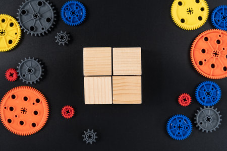 Top view of four square wooden cubes arranged in a grid and surrounded by colorful plastic gears on...