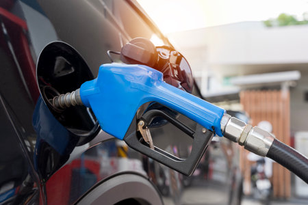Close up of fuel nozzle pumping gasoline into car tank at gas station, symbolizing energy,...