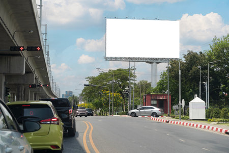 City street scene with vehicles stopping at red lights, large blank billboard, elevated railway, and...