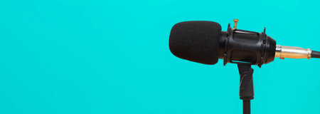 Closeup of professional black microphone on stand with turquoise background, perfect for podcast, recording, broadcasting, studio sound production, audio communication, digital media content creation.の写真素材