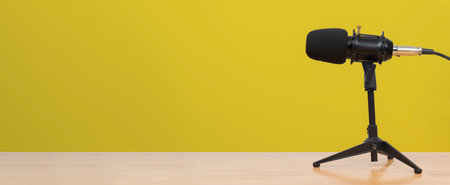 Closeup of professional black microphone on tripod stand with yellow background, suitable for...