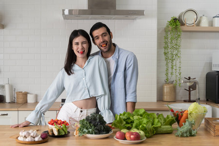 Young couple smiling in modern kitchen with fresh fruits and vegetables, representing healthy lifestyle, organic nutrition, wellness, love, family bonding, and joyful moments of cooking together.の写真素材