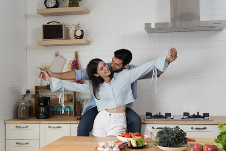 Young romantic couple dancing joyfully in modern kitchen, symbolizing love, family bonding, wellness, healthy lifestyle, organic food, togetherness, happiness, tenderness, and bright joyful emotions at homeの写真素材