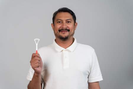 Portrait of man holding tongue cleaner for oral hygiene, concept of dental care, fresh breath, cleaning tool, personal health, prevention, wellness, lifestyle, mouth care, dental hygiene and smile.の写真素材