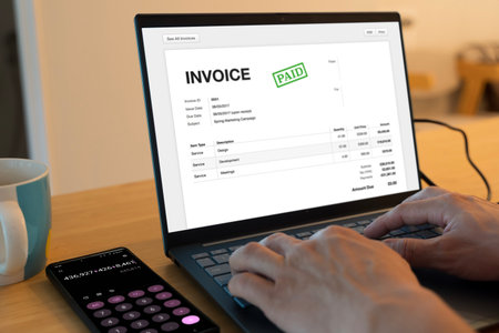 Digital invoice with paid stamp displayed on laptop screen, smartphone calculator beside coffee mug....
