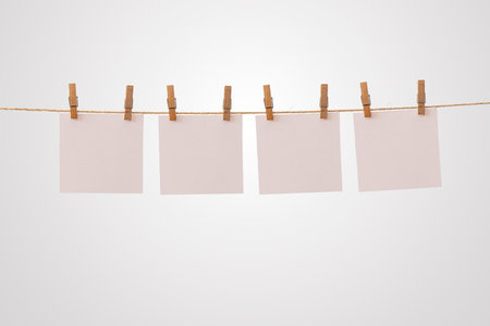 Four blank paper notes hanging on rope with wooden clothespins isolated on white background, concept for creative message, reminder, idea board, decoration, and minimalist communication designの写真素材