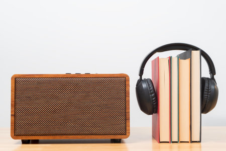 A stack of books wearing headphones sits next to a vintage wooden speaker, symbolizing audiobooks, digital learning, modern media. The reflects education, creativity and the evolution of storytelling.の写真素材