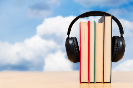 A stack of books with headphones placed on top is set against a bright blue sky, symbolizing audiobooks, digital learning, and modern education. Conveys creativity, knowledge, and accessible learning.の写真素材