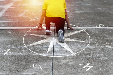 A man kneels in a starting position on a compass direction graphic, symbolizing guidance, purpose, decision-making, life direction, motivation, future goals, ambition, and the journey toward finding.の写真素材