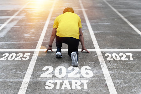 A man kneels in a starting position on a track marked 2025, 2026, and 2027, symbolizing progress, yearly goals, ambition, motivation, determination, and the journey of moving forward through success.の写真素材