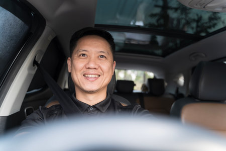 Portrait of a cheerful man driving a car with his seatbelt fastened, smiling confidently inside a...