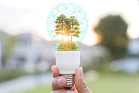 Creative eco energy concept showing a hand holding a light bulb with a growing tree inside,...