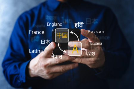 Close-up of hands using a smartphone translation app with multiple languages on screen, symbolizing multilingual communication, localization, travel, and global business technology.の写真素材