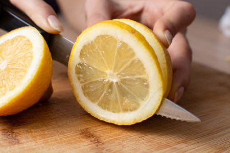 Women's hands slice a lemon in half on a wooden cutting board.の写真素材