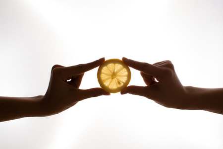 Two hands holding the slice of lemon on the white backgroundの写真素材