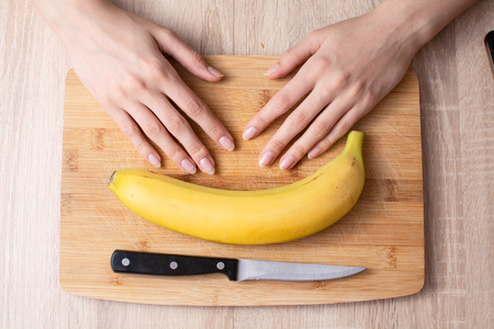 Banana, knife and wooman hands on wooden cut tableの写真素材