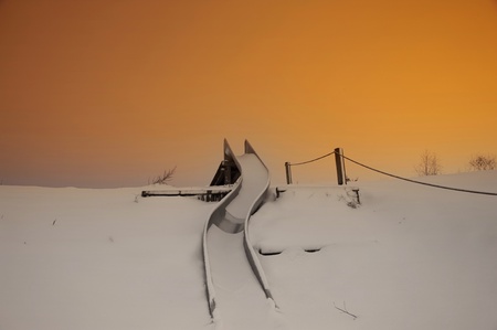 A snow covered playground slide in early winter morningの写真素材