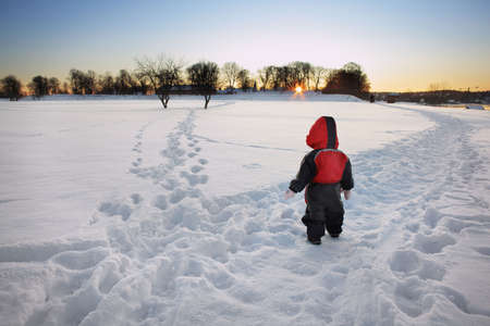 young child standing in front of separate tracks in winter landscapeの写真素材