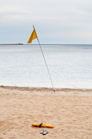 Beach Guard flag, float and flip flops in the sand of the seaの写真素材