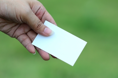 Woman's hand holding white business card in green background. の写真素材