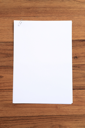 Blank white paper with clip on wood desk, top view.の写真素材