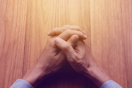 Man's hands make his hands clasped on wood table, business concept in concentration, make calm, or thinking. Top view, retro filter, vintage tone, glow light effect.の写真素材