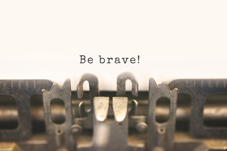 Close up of antique typewriter with message on paper Be brave! Selective focus on message, vintage filter style.の写真素材