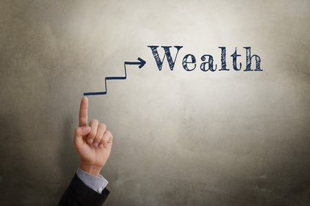 Businessman hand point at sketching arrow in direction to text Wealth, business concept of being wealthy. Glow light effect, vignette and shadow on concrete wall background.の写真素材