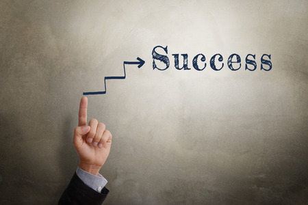 Businessman hand point at sketching arrow in direction to text Success, business concept of reaching success. Glow light effect, vignette and shadow on concrete wall background.の写真素材