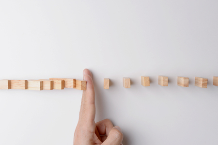 Top view of man's finger block or stop domino effect, represent with pieces of wood block on gray background with copyspace.の写真素材