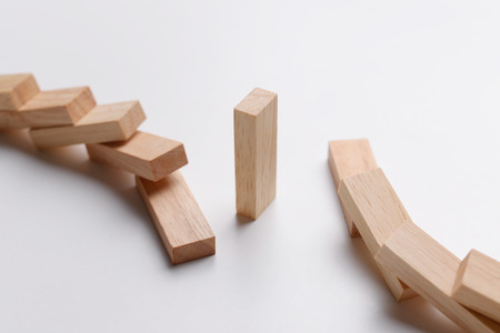 Wood block standing alone and escape from domino effect from two side, business concept in survival, standing, leadership, or escape from collapse. Selective focus on wood block in the middle.の写真素材