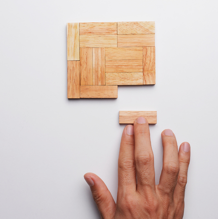 Man hand push last piece of wood block to complete the unity, metaphor to key to success. Top view, gray background.の写真素材