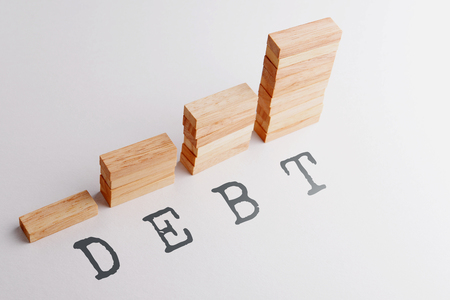 Stack of wood block in statistics graph shape with text DEBT. Business concept in rising and growing debt. Selective focus, gray background.の写真素材