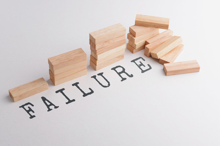 Stack of wood block in statistics graph shape failed and falling down in the end with text FAILURE, business concept metaphor to failure or destruction in the end. Selective focus, gray background.の写真素材