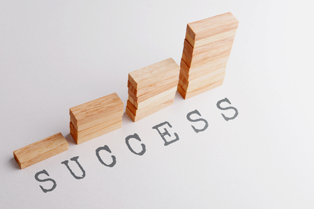 Stack of wood block in statistics graph shape with text SUCCESS. Business concept in rising and growing successful. Selective focus, gray background.の写真素材