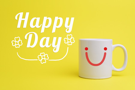 White cup of coffee on yellow background with smiley face and text Happy Day.の写真素材
