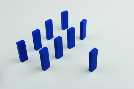 One wood block standing in front of group of wood block which standing in line or row, metaphor to leader stand in front of many follower. Business concept in leadership. Selective focus, blue color on gray background.の写真素材