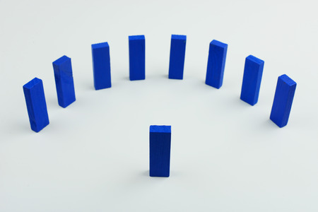 One wood block standing in front of group of wood block which standing in half circle row, metaphor to leader stand in front of many follower. Business concept in leadership. Selective focus, blue color on gray background.の写真素材