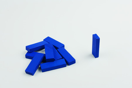 One blue wood block standing and outstanding among the collapse of other wood block, business concept metaphor to able to survive or dominant from destruction. Selective focus, blue color on gray background.の写真素材