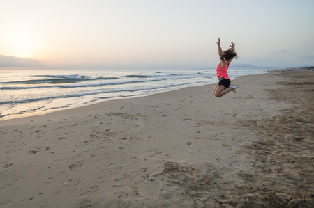 Girl jumping on the beach at sunriseの写真素材