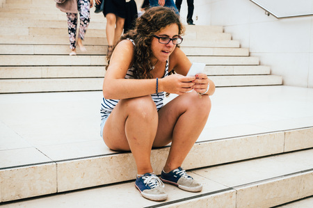 Young woman student take break at stairs in a museum and uses a smartphone (mobile phone with touchscreen)の写真素材