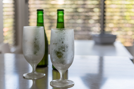 Two iced empty glasses and two green bottles of beer on backgroundの写真素材