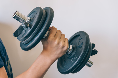Young doing exercises with dumbbell against a white wall.の写真素材