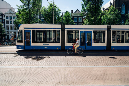 Amsterdam, Netherlands - August 1, 2016: Man riding a bicycle and tram in the street on Amsterdam.のeditorial素材