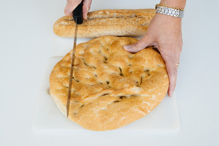 Woman hands cutting a loaf of bread on white table, food closeup. Top viewの写真素材