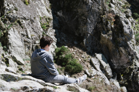 Teenage with casual clothing sitting on a rock looking out over waterfall rocks in  Madrid mountain range. Focus on foregroundの写真素材