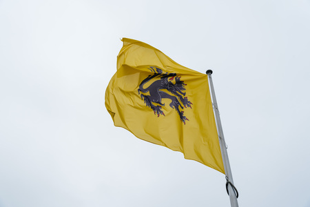 Mechelen flag on top of the tower of Cathedral. Black lion on yellow. Isolated against cloudy dayの写真素材