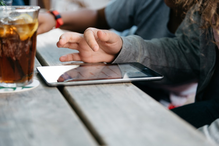 Refreshing glass of cola on wooden table in a bar while young is connected with tablet.